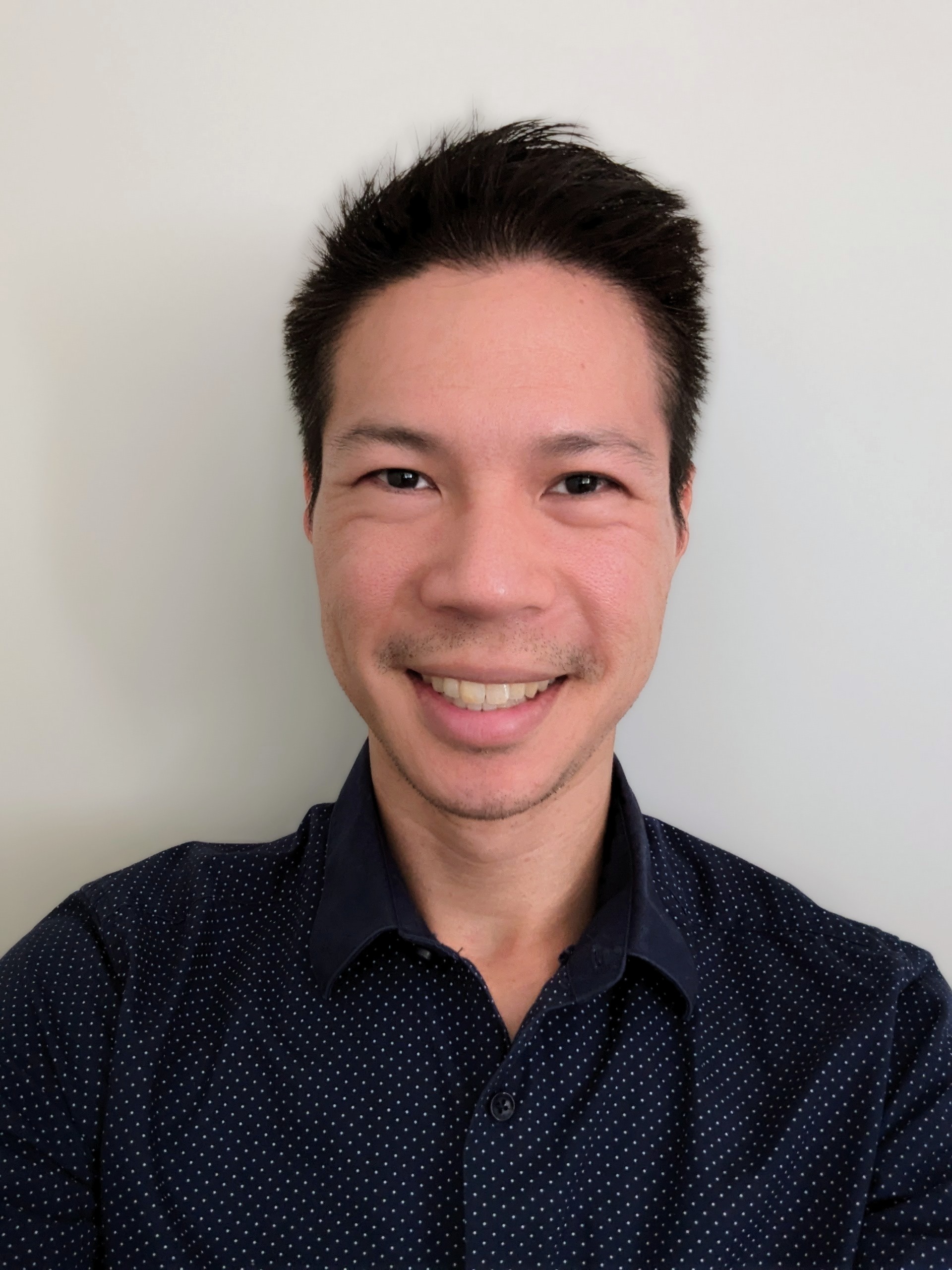 portrait photo of Francis, an Australian man with South-East Asian heritage. He is wearing a dark collared shirt, has short, black hair and dark coloured eyes and has a welcoming smile on his face
